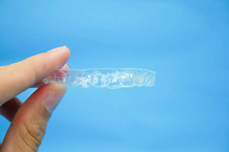 hand holding clear plastic retainer teeth that isolated on blue sky background. it's an equipment...