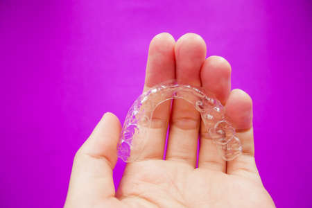 hand holding clear plastic retainer teeth that isolated on purple  background. it's an equipment for orthodontist give the patient to orthodontic surgery in dental clinic or hospitalの写真素材