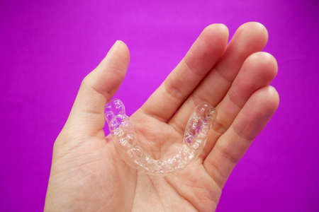 hand holding clear plastic retainer teeth that isolated on purple  background. it's an equipment for...