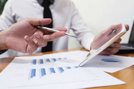 Business woman is using a pen for financial data analyzing counting on wood desk with business man,...