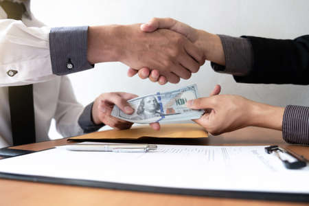 Two businessman making handshake and receiving a bribe in the office room, Bribery and corruption concept.の写真素材