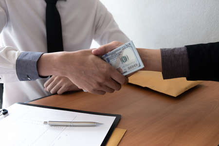 Two businessman making handshake and receiving a bribe in the office room, Bribery and corruption concept.の写真素材