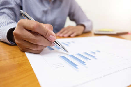 Businessman is using a pen for financial data analyzing counting on wood desk, business finances and accounting concept.の写真素材