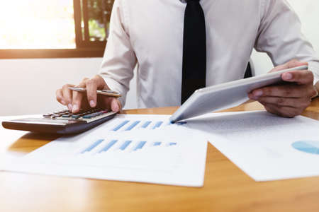 Businessman is using a calculator to calculate the numbers on wood desk, business finances and...
