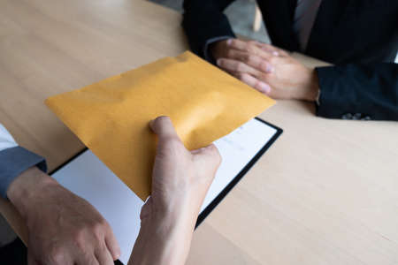 The businessman offered a bribe money in a brown envelope to another businessman sitting in front of at the office, Bribery and corruption concept.の写真素材