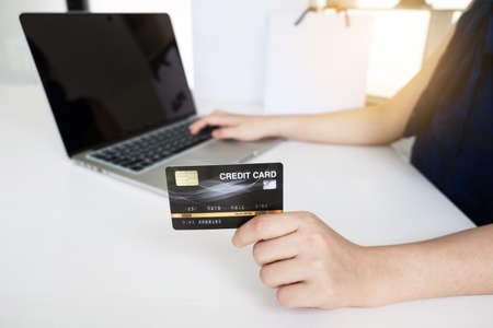 Closeup hand of women is holding a credit card and using computer notebook for shopping online.
