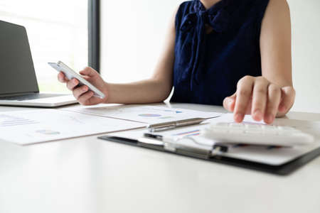 Business women is holding mobile phone and calculating revenue from graph in the office room, Finance and accounting concept.の写真素材