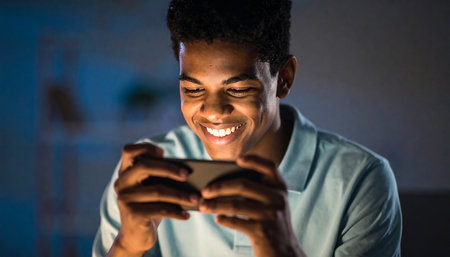 Smiling african american man using mobile phone in dark roomの素材
