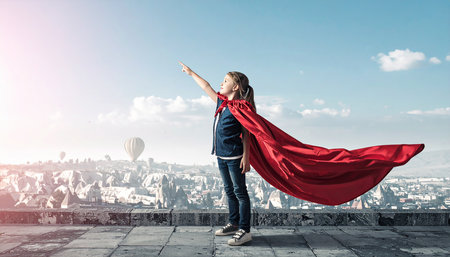 Little confident girl in mask and cape plays cool superhero. Mixed mediaの素材