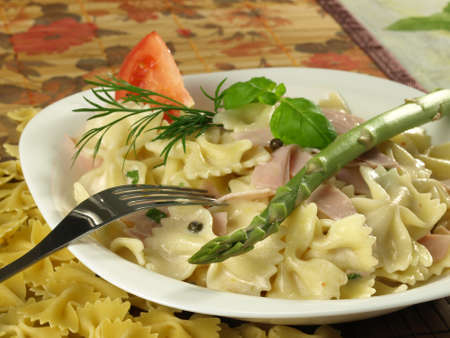 Farfalle pasta with ham, asparagus, basil and tomato on a plateの写真素材