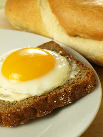 Sunny side up egg on a slice of bread on a plate with a French loaf in the background