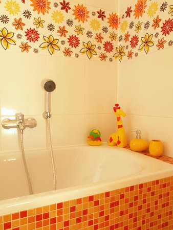 Closeup of a mosaic bath with a shower, yellow children toys and flower tiles