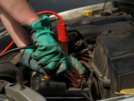 Charging battery in car by mechanic in glovesの写真素材