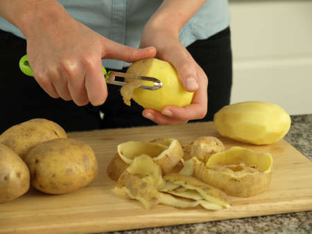 Preparing dinner: hands peeling potatoes for boilingの写真素材