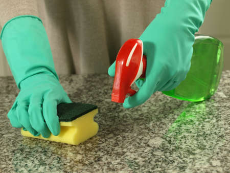 Housewife cleaning up a kitchen top with sponge and spray