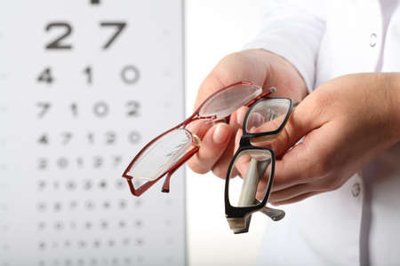 Optometrist holding two pair of glasses, eye chart