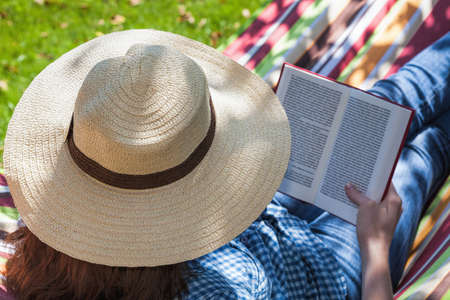 A woman with a hat reading on a striped deckchairの写真素材