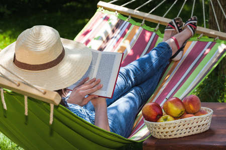 A woman relaxing on a hammock with a novelの写真素材