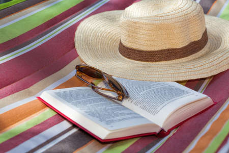 Book and straw hat on a colorful hammockの写真素材