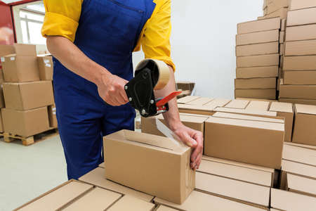 Factory worker with packing tape gun dispenser finishing a deliveryの写真素材