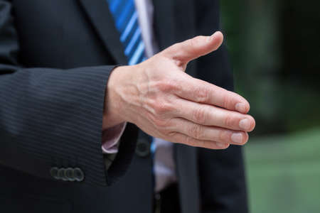 Businessman hand just before a handshake on green natural backgroundの写真素材