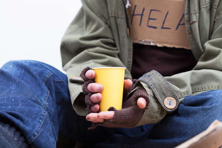 Hands of homeless person holding a yellow, paper cupの写真素材