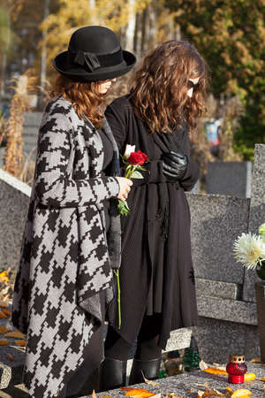 Two women standing above grave on sunny autumn dayの写真素材