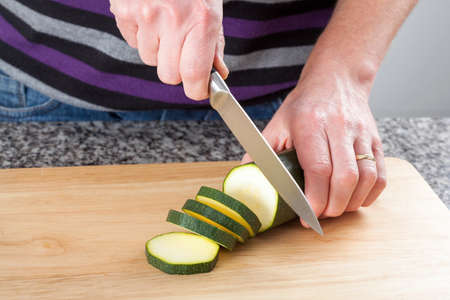 Man cutting a fresh zucchini on the brown boardの写真素材