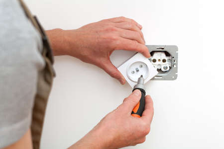 Electrician repairing electrical socket on white wallの写真素材