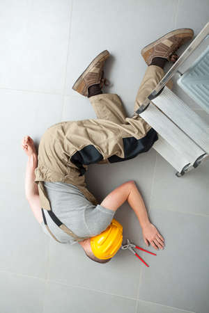 Worker lying on grey floor near to ladder unconsciousの写真素材