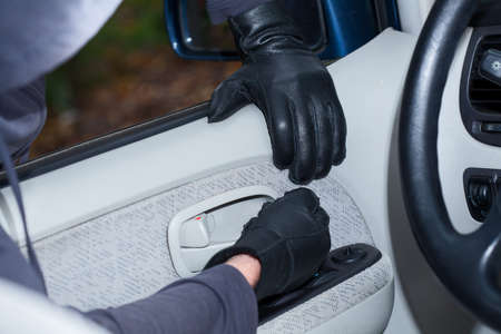 Thief wearing black gloves breaking into a car