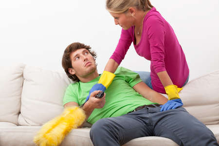 Woman with cleaning duster disturbing her husband in watching tvの写真素材