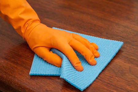 A man with a glove polishing a woodentable with a rag