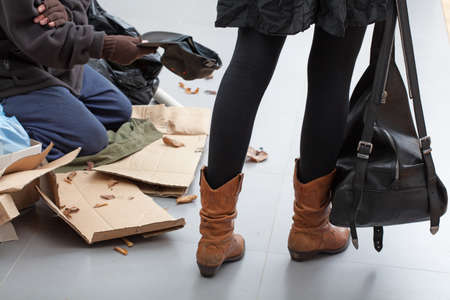 Beggar sitting on a crowded street passed by womenの写真素材