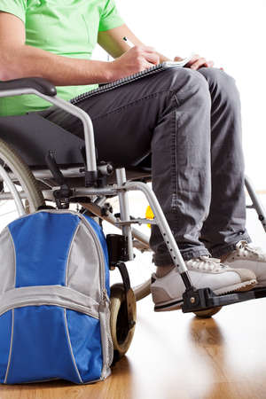 A student on a wheelchair with a backpack writing in his notebook