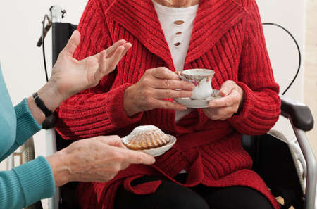 Elder woman on wheelchair has a nice friend visit for coffee and cakeの写真素材