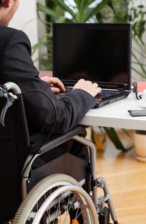 Young businessman on wheelchair wearing suit and working on computer