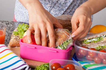 A closeup of hands packing snacks into a pink lunch boxの写真素材