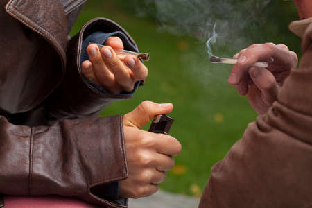 Close up of hands holding two burninig joints and thick smokeの写真素材