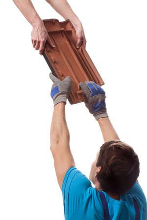 A closeup of builders passing an orange piece of tileの写真素材
