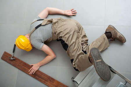 Manual worker dressed in work clothes lying unconscious on the grey floorの写真素材