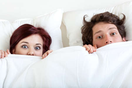Couple with funny faces under the sheetの写真素材