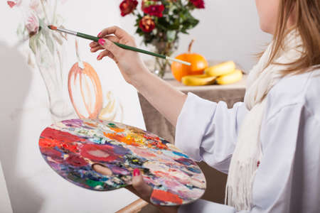Young talented woman painting a nature on white canvasの写真素材