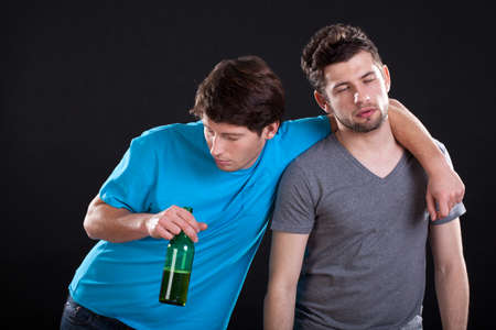 Two men friends standing drunk with a bottle of beer