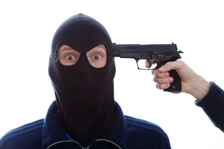 A closeup of a masked terrified burglar with a pistol against his headの写真素材