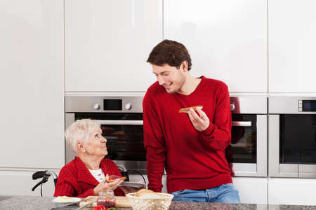 Grandson eating sandwiches with his disabled grandmaの写真素材