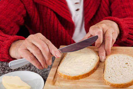 Elderly woman spreading bread with butter for breakfastの写真素材