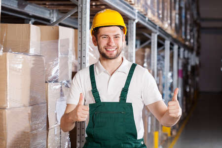 Happy warehouse worker in yellow hardhat showing ok signの写真素材