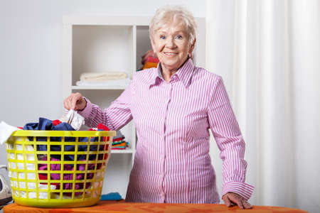 Senior lady wearing shirt during folding laundryの写真素材