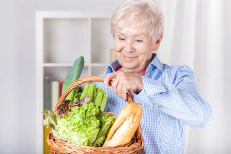 Elderly woman with shopping basket at homeの写真素材